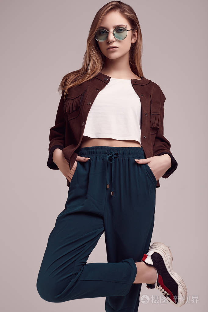 照片 可爱的十几岁女孩的肖像在时尚夹克和彩色眼镜摆在灰色背景上.