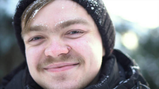 英俊开朗的男人的肖像, 留着胡子, 穿着冬衣, 脸上有雪。在阳光明媚的冬日里, 蓝眼睛微笑着的金发碧眼的男人