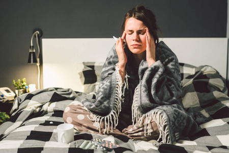 年轻的白人妇女坐在家里的卧室床包裹着全身的高烧, 发烧后头痛, 用滴
