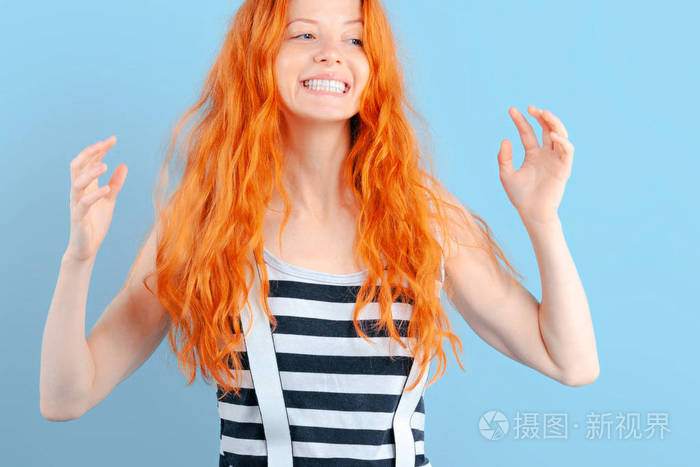 红头发的女孩笑着举起双手在蓝色的背景上快乐和惊喜