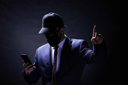 手机盗窃黑色背景下带手机的专业黑客. 互联网盗窃概念照片
