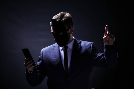 手机盗窃黑色背景下带手机的专业黑客. 互联网盗窃概念照片