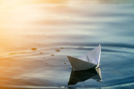 关闭简单的白色折纸船静静地漂浮在蓝色清澈的河流或海水下明亮的夏季天空。 自由梦想和幻想概念共空间背景。
