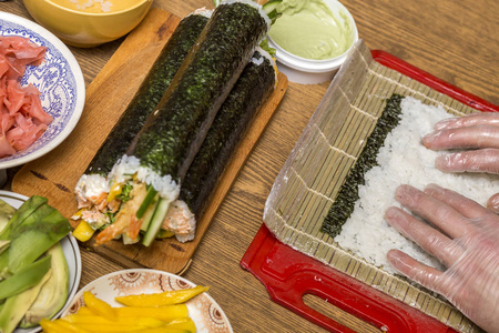 制作寿司和卷的过程。 关闭男子厨师手准备传统的日本食物在家里或餐厅在厨房的桌子上。