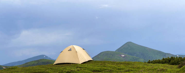 夏天阳光明媚。 小旅游帐篷在草谷上，在遥远的雾蒙蒙的青山上，在晴朗的蓝天背景下。 旅游徒步露营和自然美景的概念。