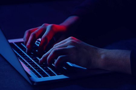 有笔记本电脑的专业黑客坐在桌子旁，特写镜头