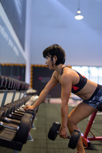 年轻美丽的亚洲女人在健身房做哑铃排