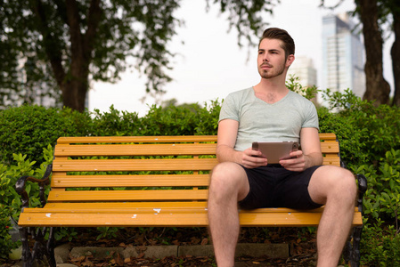 年轻人坐在公园里, 一边使用数字平板电脑思考