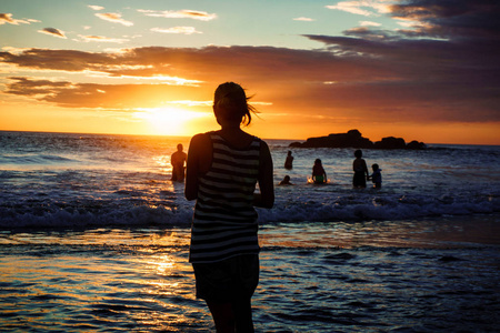 日落海滩上的女人剪影，女孩在夏日的阳光下走在海边