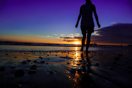 下走日落海滩上的女人剪影,女孩在夏日的阳光下走在海边照片