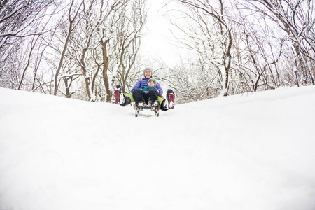 母亲带着一个孩子骑在雪橇上。 一个女人和她的儿子坐着雪橇下山。 这个男孩花时间和他的父母在一起。 有趣的寒假。