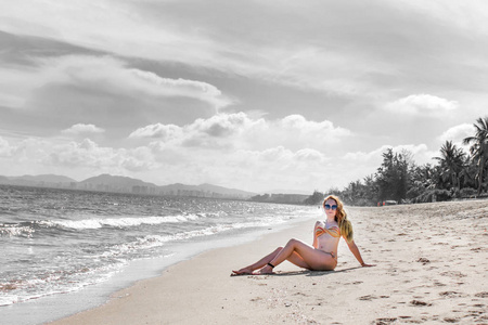 穿比基尼的漂亮女孩在荒无人烟的海滩上摆姿势。 白沙绿松石海和一个年轻的女孩。 阳光明媚的一天