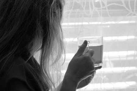 女人在家喝茶。 年轻女孩享受热茶。 一位年轻女子在窗户附近的家喝早茶的肖像。 黑白摄影。