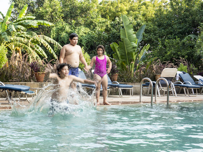 三个快乐的青少年兄弟姐妹正在度假村跳进游泳池。 暑假假期共度共谋假期