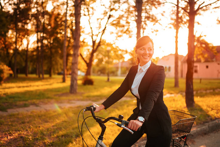年轻微笑的女人下班后骑自行车穿过公园。