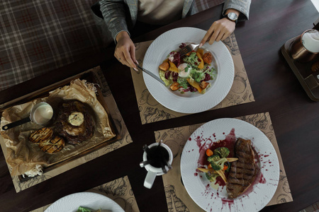 一套菜来自牛肉烤蔬菜沙拉与浸蛋和条纹牛排酒酱。 餐厅里坐在木桌旁的女人的俯视图