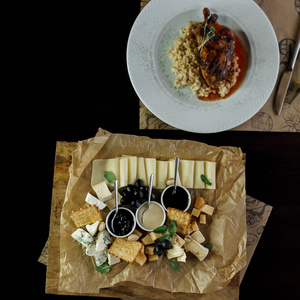 奶酪盘立在一家餐馆的木桌上，旁边是一条酱鸭腿。 简单美味的小吃。 咖啡馆里有用的午餐。 带食物的桌子的顶部视图。