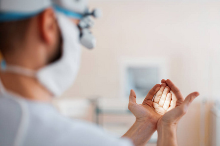 医生神经外科医生戴着专业放大镜的医用口罩，双手检查双眼百叶窗。 手术中的准备。 背面视图