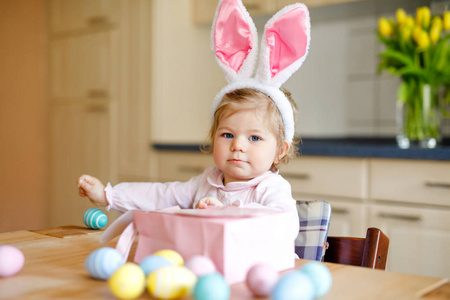 可爱的幼儿女孩穿着复活节兔子耳朵玩彩色彩蛋。快乐的婴儿打开礼物。可爱的健康微笑的孩子在粉红色的衣服享受家庭假期