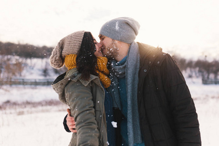 快乐的女人和男人亲吻和拥抱在一起度过彼此的雪生活冬天。 肖像美妙的年轻夫妇戴着时尚的羊毛帽和围巾。