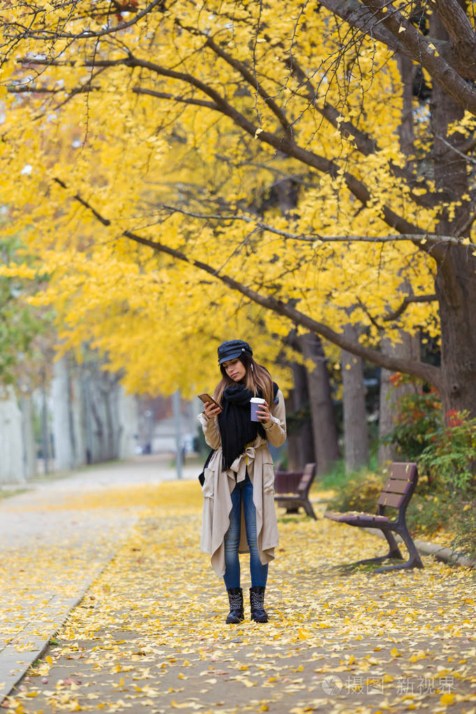 秋天在公园里散步时一个漂亮的年轻女人用她的手机拍摄的照片