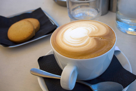 棕色的酱油卡普奇诺拿铁艺术在白色杯和酱油加饼干.