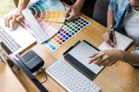 团队年轻的同事创意平面设计师工作的颜色选择和绘制图形平板在工作场所，颜色样本图表选择着色。