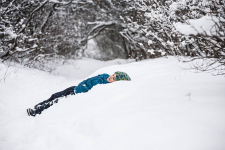 那个男孩躺在雪地里。 孩子穿过冬天的森林。 寒假。 这孩子做了个雪天使。