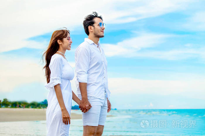 年轻的一对相爱的年轻夫妇在蓝天的海滩上携手共进幸福的微笑年轻的