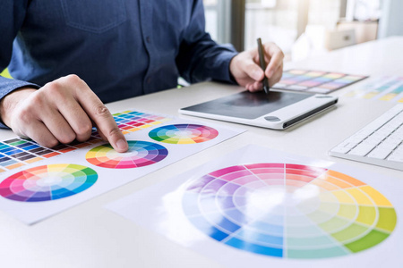 男性创意平面设计师工作的颜色选择和彩色样本绘制在图形平板在工作场所与工作工具和附件。