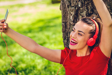 年轻快乐的女人通过耳机和智能手机在户外听音乐
