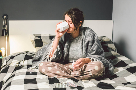 年轻美丽的白种人妇女患感冒，高热，在家里卧床。 这个女孩用一杯水吃头痛药，一颗苦药丸是歪的。