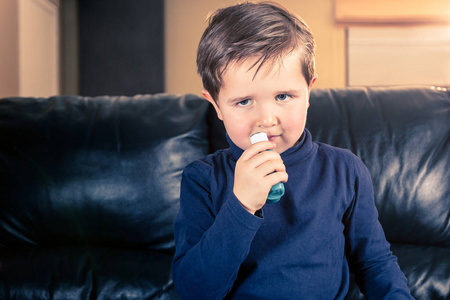可爱的5岁幼儿拿着他的哮喘吸入器坐在黑色皮革沙发上