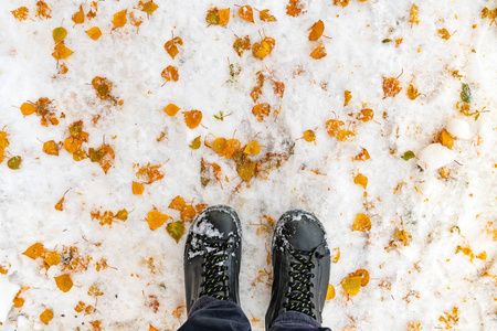 穿着靴子的男足站在冬天，白雪覆盖着黄叶