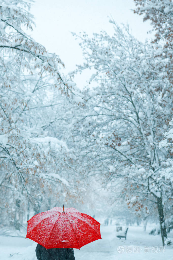 在雪地里打着红伞的女人享受着冬季的第一场降雪