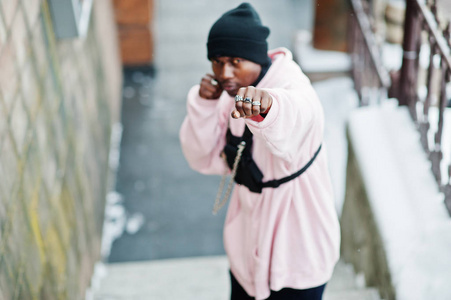 时尚的城市风格非裔美国人穿着粉红色连帽衫在冬天和拳击手摆姿势。