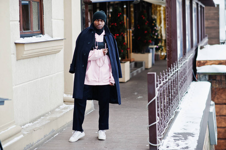时尚的城市风格，非裔美国人，穿着黑色外套和帽子，粉红色帽衫，在冬天摆姿势。