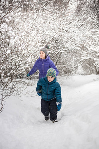 这个男孩在一条下雪的小路上逃离了他的母亲。那个男孩和他妈妈在一条覆盖着雪的森林小径上散步。寒假。一个孩子正在和他的母亲玩。