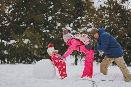 家庭妇女男人小女孩穿着温暖的衣服，在雪地公园或户外森林里堆雪人互相推搡。 假日的冬季乐趣休闲。 家庭生活方式观念