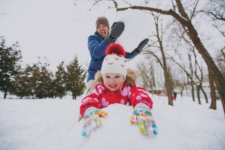 开朗的家庭爸爸在冬天穿暖和的衣服，拿着大雪球，小女孩在公园或森林里玩雪。 假日的冬季乐趣休闲。 家庭生活方式观念