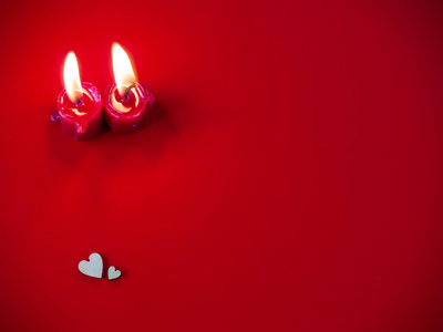 爱的概念红烛点燃，两颗木制的心有红色的背景