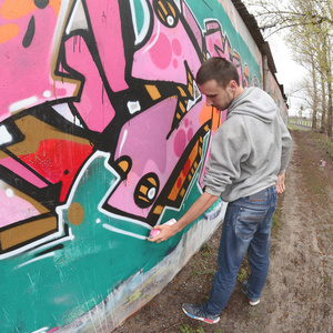 一个穿灰色连帽衫的年轻人在雨天在墙上画粉红色和绿色的涂鸦。菲什耶