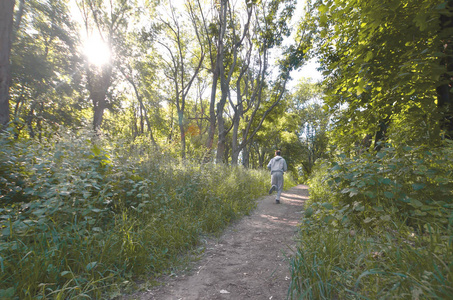 一个穿灰色运动服的年轻人沿着树林里的小路跑。 户外运动