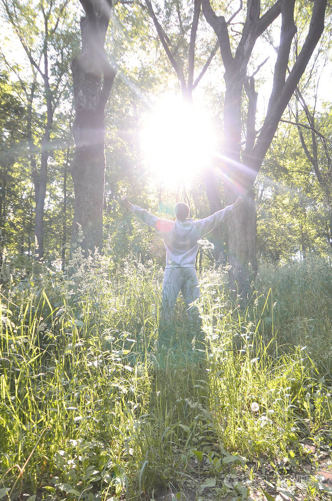 一个穿灰色运动服的年轻人在森林里的树木中享受着太阳的升起.