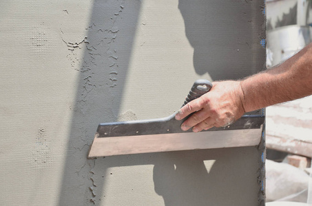 一个老手工工人的手与墙壁抹灰工具翻新房子。 泥塑工用抹子和石膏翻新室外墙壁和角落。 墙壁绝缘。 建筑整理工程
