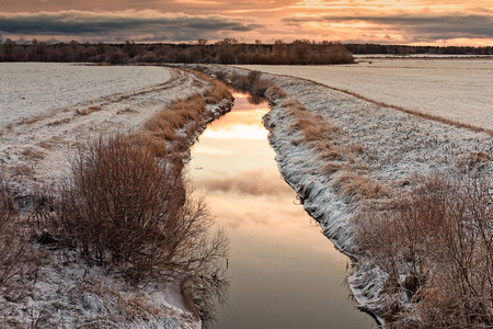 一条小河流经芬兰北部的田野。 早晨的太阳使天空琥珀色，光线反射在静水上。