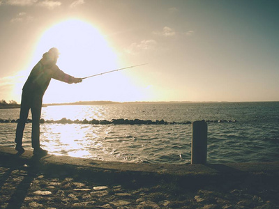 渔夫带着帽子，戴着鱼竿，戴着海痣。站在海水之上的人在日落时分捕鱼