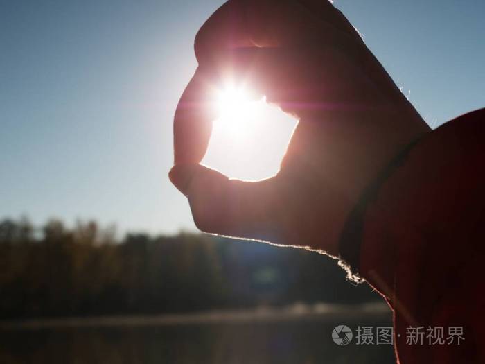 日落时双手抓太阳. 雌性手指把太阳举在湖面上.