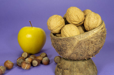 天然椰子壳杯中的全核桃仁和紫色背景上的黄苹果