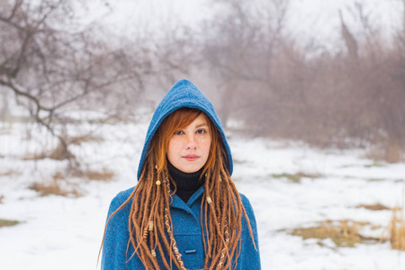 穿着复古蓝色外套的年轻女人在冬天的雾中公园散步，雪和树背景，幻想或仙女的概念